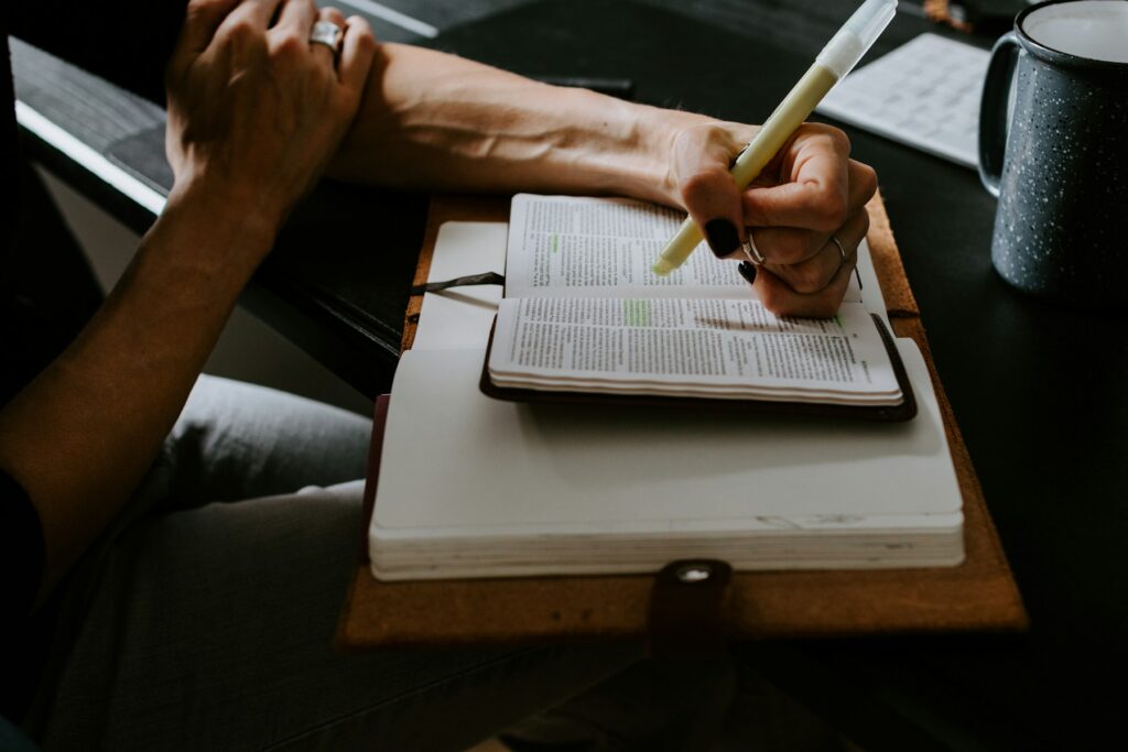 Dłoń zaznaczająca fragment otwartej Biblii leżącej na notatniku.